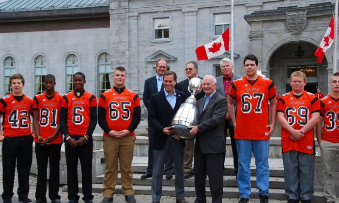 Canadian Football League (CFL) Commissioner Mark Cohon (L) and Governor General of Canada David Johnston hold the Grey Cup outside Rideau Hall, the Governor General's official residence, alongside members of the Orleans Bengals Football Club and former CFL greats, on Oct. 21, 2012. The trophy, awarded to the best Canadian professional football team, will be on display to the public at Rideau Hall from Oct. 21 to Oct. 24, 2012. (Jonathan Ren/The Epoch Times)