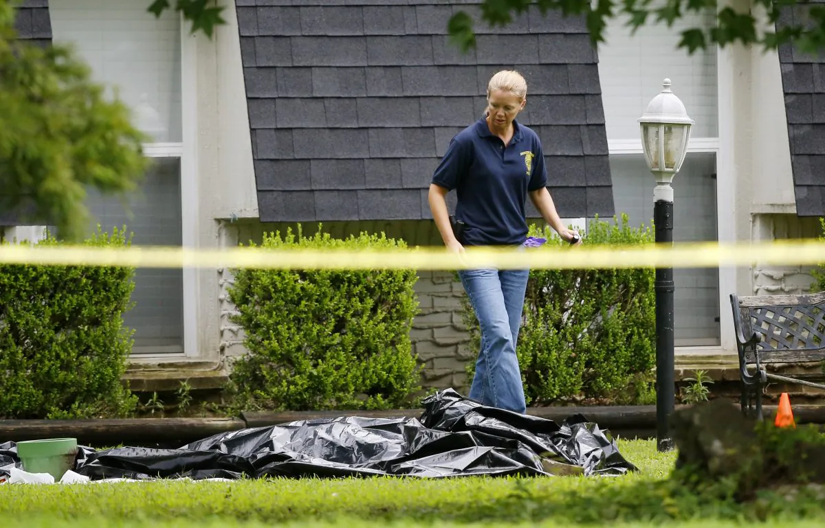 An investigator walks past a tarp covering a body in the front yard of a house in Broken Arrow, Okla., Thursday, July 23, 2015. (AP Photo/Sue Ogrocki)
