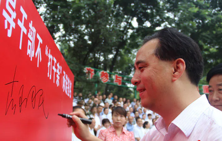 Local Chinese official Hu Guomin signs a board with an oath to end fictive kinship amongst Communist Party members in Qingshen County, Sichuan Province on July 22, 2015. (Screen shot/China Radio International)