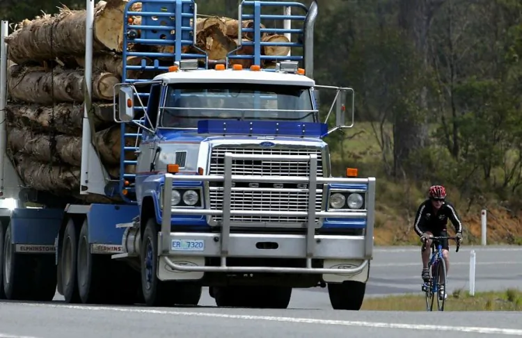 TASMANIA, AUSTRALIA: Logging trucks share the road with a cyclist. Conservation 'peace deal' with logging industry at stalemate. (Clive Mason/Getty Images).