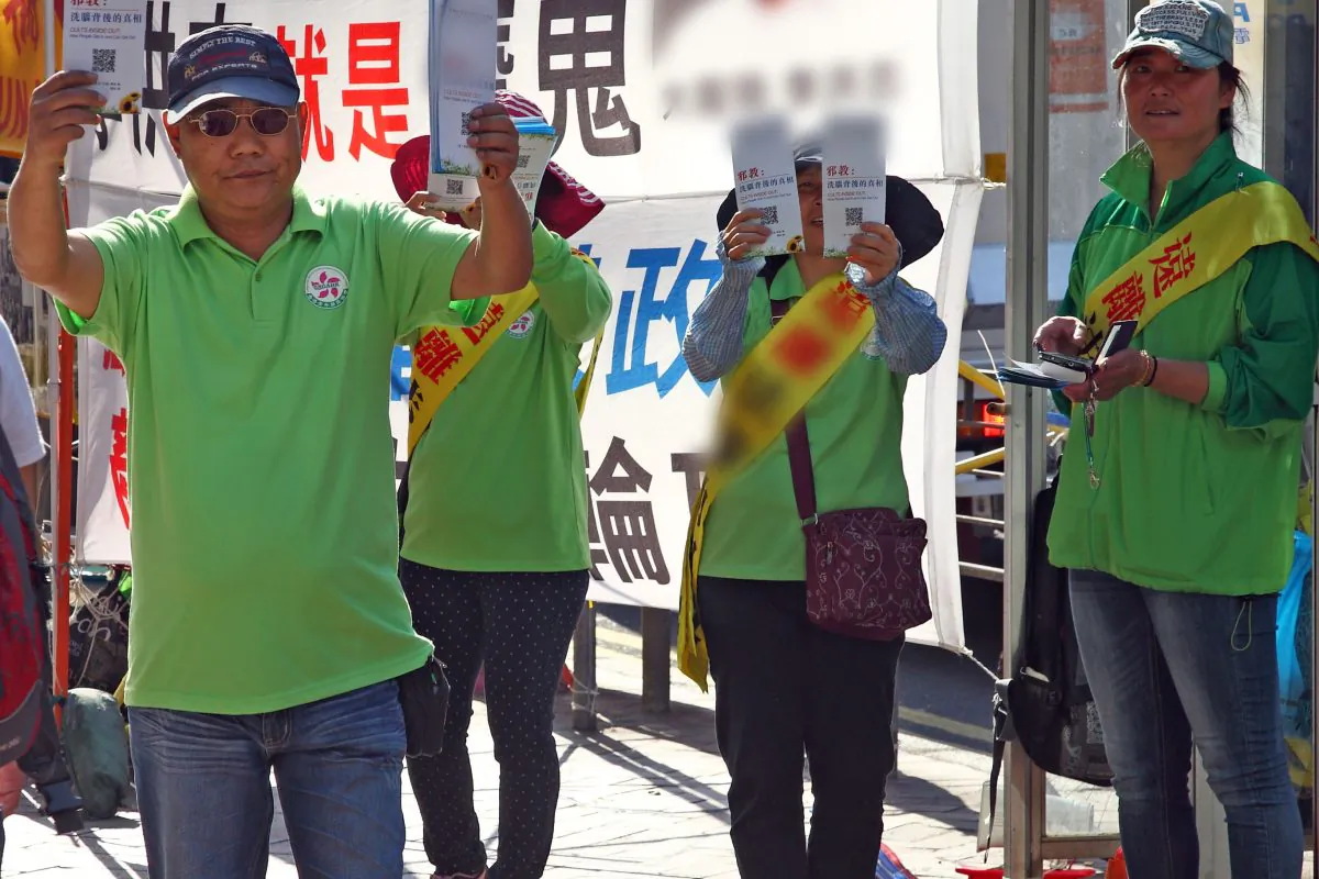CCP supported group Hong Kong Youth Care Association (HKYCA) set information booths next to Falun Gong’s and use their own banners, loudspeakers and flyers to castigate and mock Falun Gong. In the photo, the HKYCA members in green are holding slanderous flyers at Mong Kok on April 16, 2015. (Epoch Times)