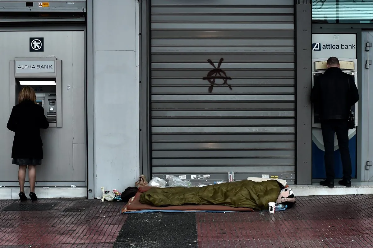 A homeless man sleeps outside a bank as people withdraw cash from ATMs in central Athens on March 13, 2015. (Aris Messinis/AFP/Getty Images)