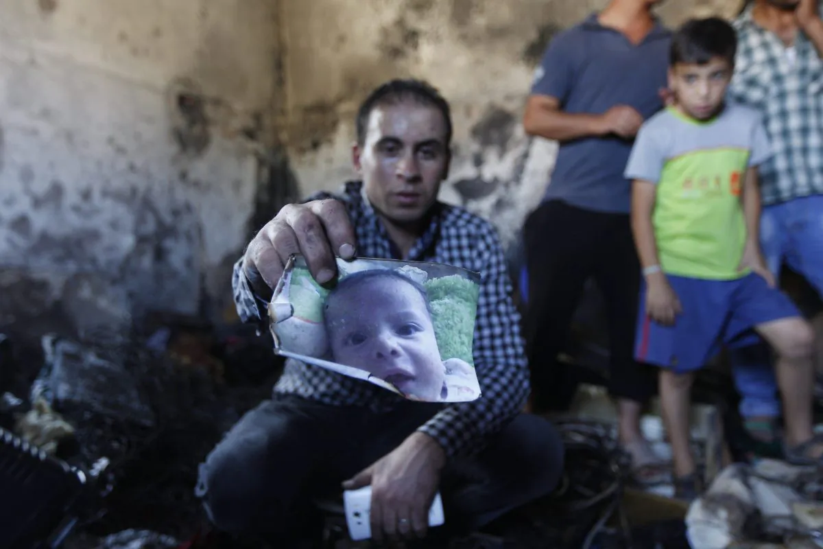 A relative holds up a photo of a one-and-a-half year old boy, Ali Dawabsheh, in a house that had been torched in a suspected attack by Jewish settlers in Duma village near the West Bank city of Nablus, Friday, July 31, 2015. (AP Photo/Majdi Mohammed)