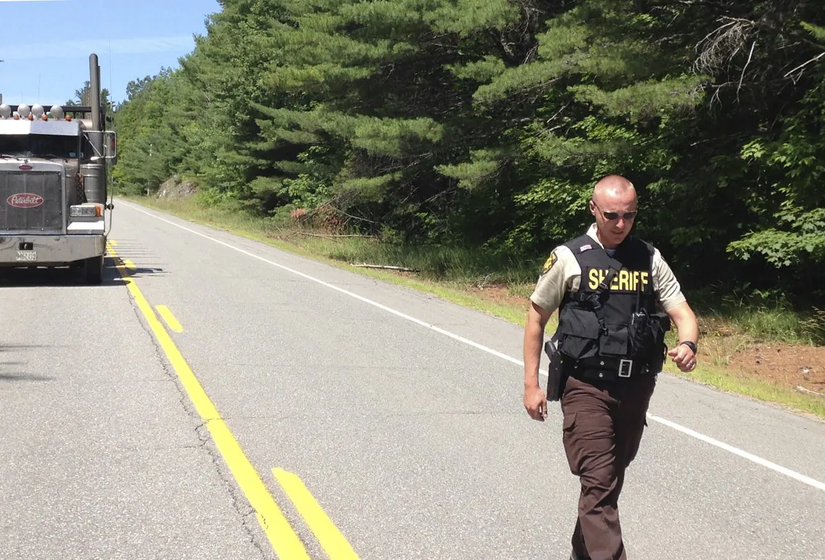 A Penobscot County Sheriff deputy walks along a road at a checkpoint Friday, July 17, 2015, in Lee, Maine.  (AP Photo/Alanna Durkin)