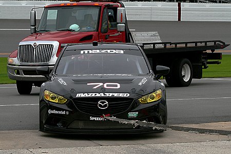 The #70 SpeedSource Mazda6 returns to the garages on a tow-rope after experiencing engine failure on track. The crew was able to get the car going again for the night test session. (Chris Jasurek/The Epoch Times)