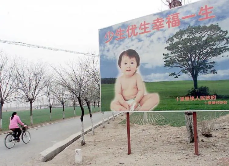 A woman cycles pass a billboard encouraging couples to have only one child, along a road leading to a village in the suburb of Beijing, 25 March 2001. A Party official recently proposed moving to a two-child policy in some regions. (Goh Chai Hin/AFP/Getty Images)