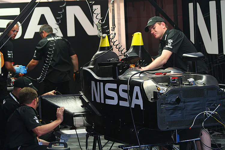 The DeltaWing’s crew works to repair the damaged prototype. The driver’s roll hoop shows the damage it sustained when it hit the pavement. (James Fish/The Epoch Times)