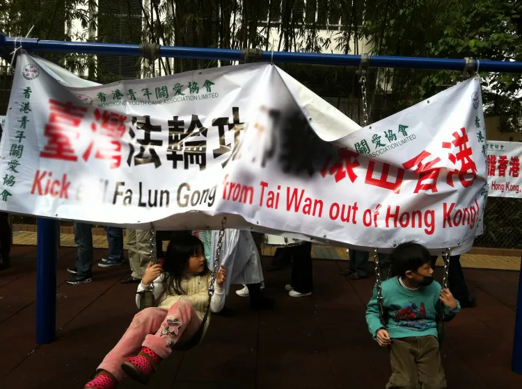Falun Gong practitioners are seen meditating at their information site at Star Ferry in Hong Kong on Feb. 13, 2013. A rack of banners subsequently erected by the Hong Kong Youth Care Association blocks passerby from seeing the practitioners' site. The raised tile at the base of the Association's banners is a pathway meant for the blind. (Epoch Times)