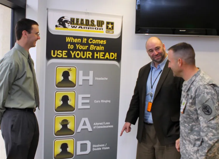 Dr. Bart Winter, Fort Sill Traumatic Brain Injury clinic physician, examines a "H.E.A.D.S. UP Warrior" banner that lists the signs of a concussion with Dr. Jason Albano, TBI neuropsychologist, and Public Health Service Lt. Dennis Ward, TBI program director. Staff members at the clinic work with soldiers wounded by improvised explosive device blasts or other head trauma in combat. (Ben Sherman, Fort Sill)