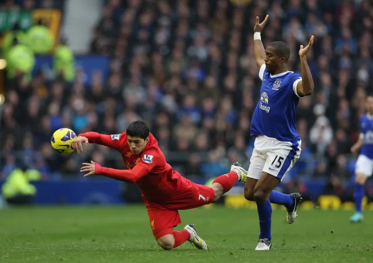 Liverpool’s Luis Suarez (L) goes down in a challenge from Everton’s Sylvain Distin in Sunday’s Merseyside derby at Goodison Park. (Clive Brunskill/Getty Images)