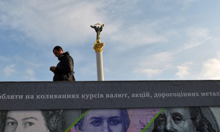 A man stands next to an advertising placard showing British pounds, US dollars, and Ukrainian hryvnia banknotes on a warm autumn day in the Kyiv, Ukraine, on Nov. 12, 2012. (Sergei Supinsky/AFP/Getty Images)