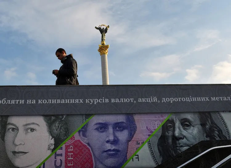 A man stands next to an advertising placard showing British pounds, US dollars, and Ukrainian hryvnia banknotes on a warm autumn day in the Kyiv, Ukraine, on Nov. 12, 2012. (Sergei Supinsky/AFP/Getty Images)