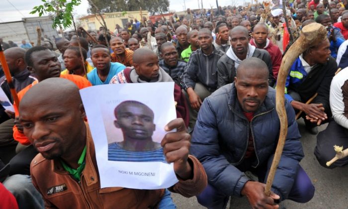 A miner carries a photo of a killed miner as thousands of striking workers singing and carrying sticks march on a South African mine in Marikana on Sept. 5 as police were accused of shooting miners in cold blood during a crackdown that killed 34. (Alexander Joe/AFP/GettyImages)