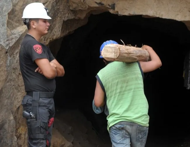 A policeman stands guard as a rescuer carries a timber post into the mine for use as a tunnel support during an operation to rescue nine miners at the Cabeza de Negro copper mine. (Cris Bouroncle/AFP/Getty Images)