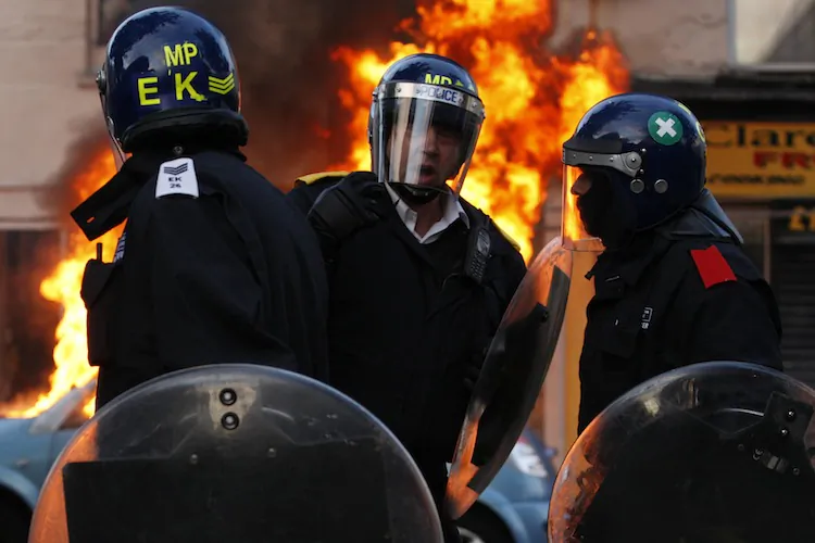 Riot police talk in front of a burning car during riots in Clarence Road, Hackney on August 8, 2011 in London, England. (Dan Istitene/Getty Images)