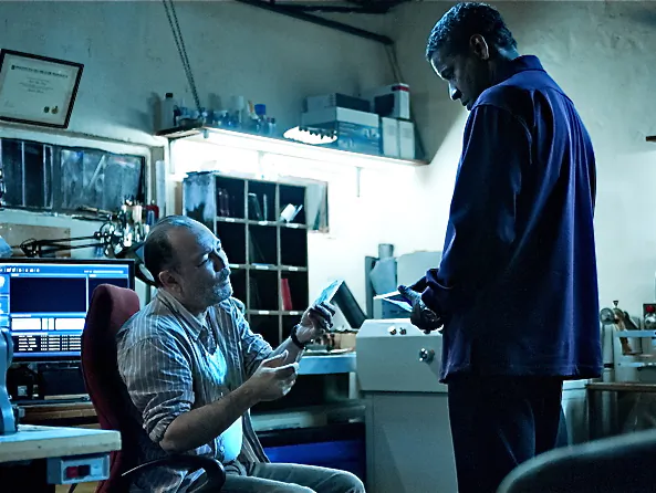 Ruben Blades prepares documents for Denzel Washington (R) in the action-thriller “Safe House,” a film about a young CIA agent on the run with his charge. (Universal Pictures)