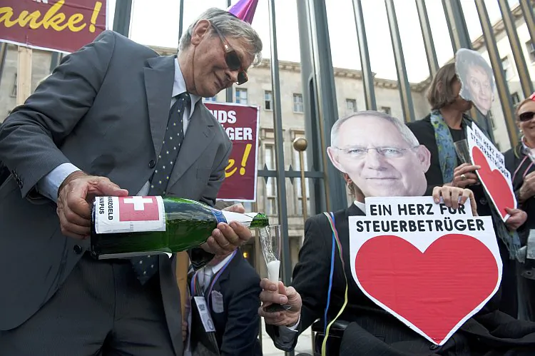 A demonstrator carrying a bottle of 'Schwarzgeld' (dirty money) champagne pours a glass for an activist posing as German Finance Minister Wolfgang Schäuble holding a sign saying, “A Heart for Tax Criminals” during a protest in Berlin Sept. 21, 2011. The protesters allege that a proposed tax deal would amount to whitewashing tax evaders. (John MacDougall/AFP/Getty Images)