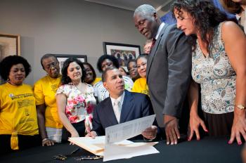 LONG TIME COMING: Members of the Domestic Workers United (DWU) in yellow t-shirts and DWU Director Priscilla Gonz���¡les look on while Gov. Paterson signs the nation's first Domestic Workers' Bill of Rights. (The Epoch Times)