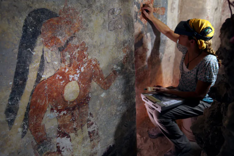 Conservator Angelyn Bass cleans and stabilizes the surface of a wall of a Maya house that dates to the 9th century A.D. The figure of a man who may have been the town scribe appears on the wall to her left. The research is supported by the National Geographic Society. (Tyrone Turner © 2012 National Geographic)
