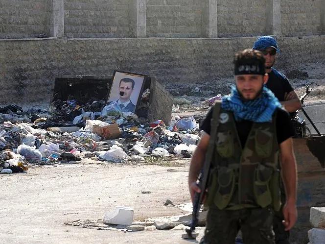 Fighters from the Syrian opposition guard a checkpoint during clashes with forces loyal to President Bashar al-Assad (portrait), in the center of Syria's restive northern city of Aleppo on July 25. (Bulent Kilic/AFP/GettyImages)