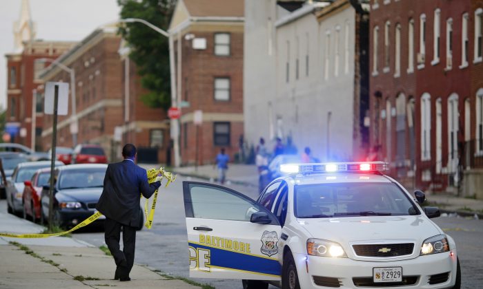 A member of the Baltimore Police Department removes crime scene tape on July 30, 2015, from a corner where a victim of a shooting was discovered. (Patrick Semansky/AP Photo)