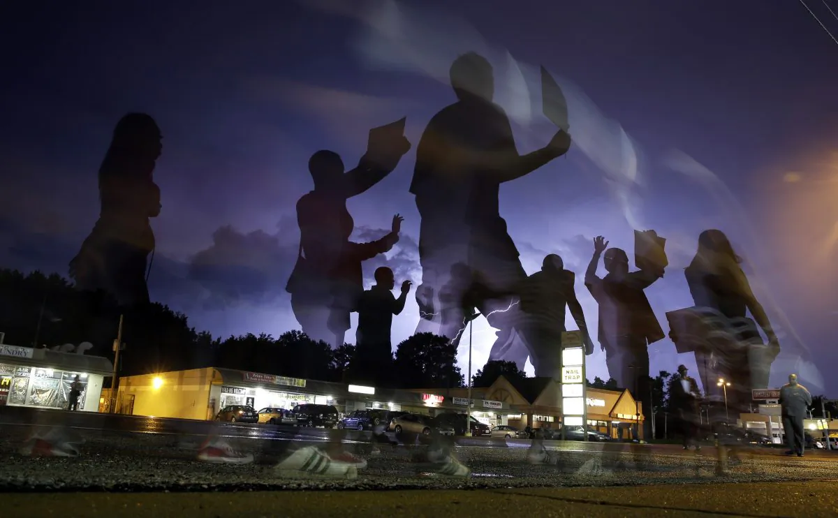 Photo taken with a long exposure, protesters march in the street as lightning flashes in the distance in Ferguson, Mo, Aug. 20, 2014. (AP Photo/Jeff Roberson)