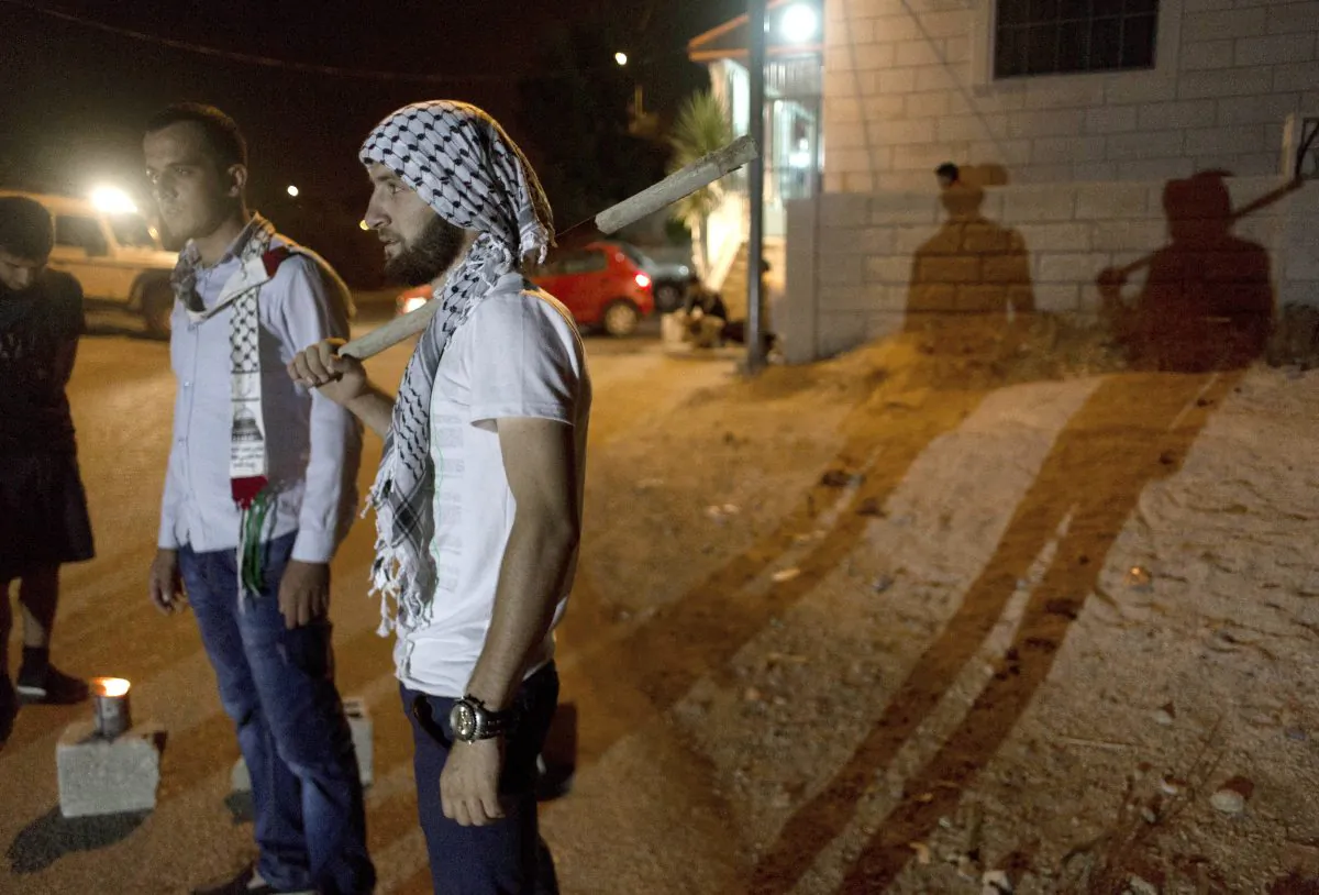 In this Tuesday, Aug. 4, 2015 photo, Palestinian villagers stand guard at the entrance of the West Bank village of al-Jab'a, near Bethlehem. The Residents of the village formed groups of defense volunteers to guard themselves from attacks of Israeli settlers. (AP Photo/Nasser Nasser)