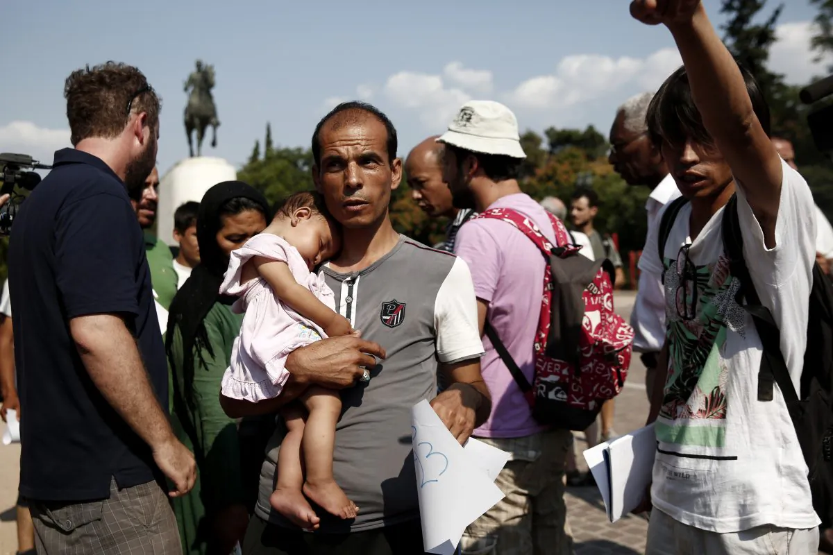 A migrant with his child makes his way to board a fire brigade bus to be transferred from a park to an organized camp which has been set up by the Greek state a few miles from the centre of Athens, Sunday, Aug. 16, 2015. Greek authorities say they have started resettling migrants living in tents in a park in the capital Athens, but many are wary of such a move and have moved to directions unknown thus far. (AP Photo/Yorgos Karahalis)