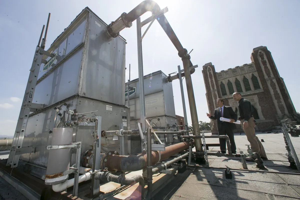 In this Friday, Aug. 7, 2015 photo, Christos Chrysiliou, left, director of architectural and engineering, Los Angeles Unified School District, LAUSD, and Peter Yee, senior project manager, examine an outdated central air conditioner unit at the John Marshall High School in Los Angeles. (AP Photo/Damian Dovarganes)