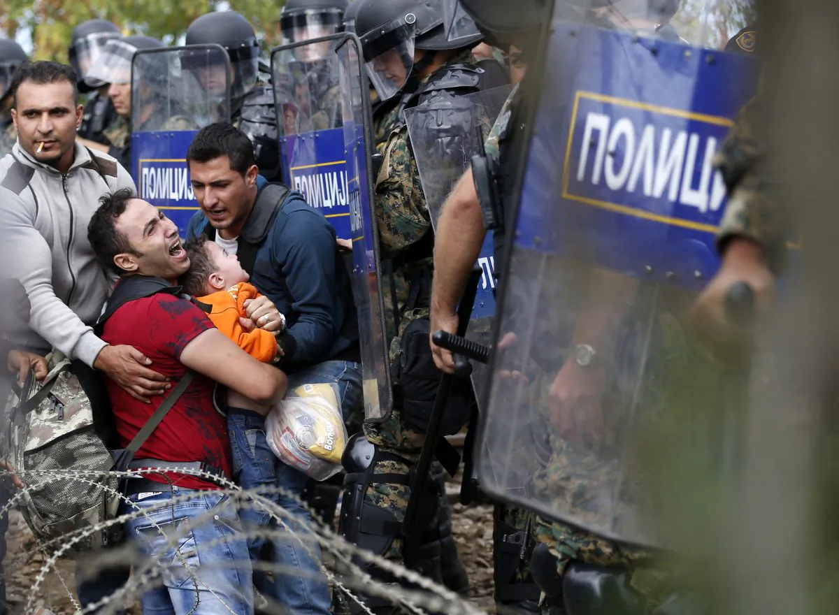 Migrant men help a fellow migrant man holding a boy as they are stuck between Macedonian riot police officers and migrants during a clash near the border train station of Idomeni, northern Greece, as they wait to be allowed by the Macedonian police to cross the border from Greece to Macedonia, Friday, Aug. 21, 2015.   (AP Photo/Darko Vojinovic)