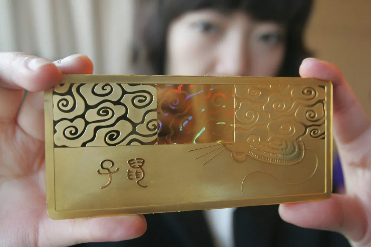 A Chinese staff shows off a gold bullion with a design of the rat in Beijing 17 December 2007. (STR/AFP/Getty Images)