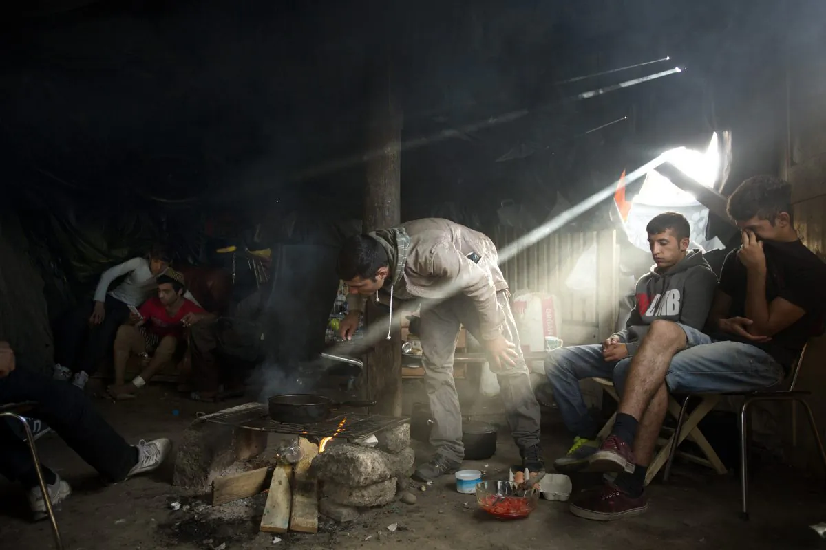 In this Sunday, Aug. 9, 2015, file photo, Afghan migrants stay inside a tent as they cook food at a camp set near Calais, northern France. (AP Photo/Emilio Morenatti)