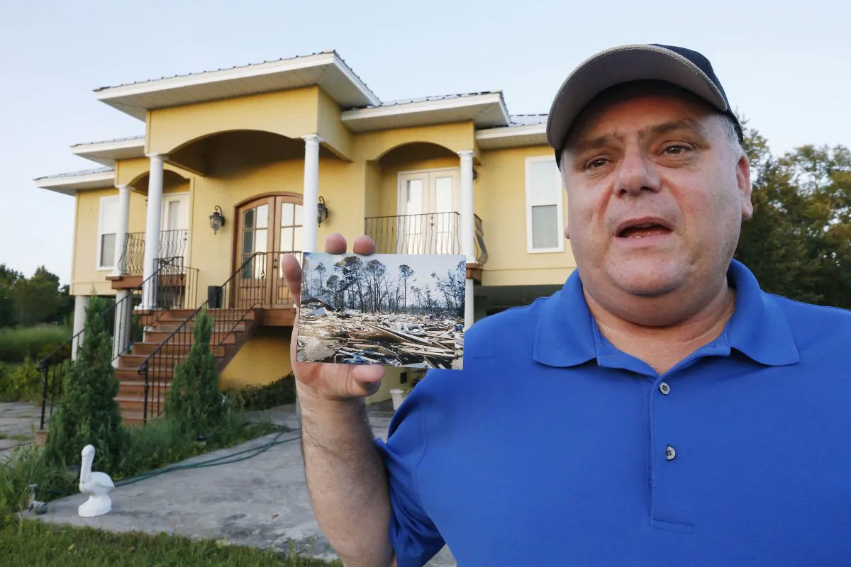 In this July 23, 2015 photo, Efrem Garza stands before his new home built on the lot of his previous house that was destroyed by Hurricane Katrina and holds a photograph taken by a friend of the remains of that house on South Seashore Avenue in Long Beach, Miss. (AP Photo/Rogelio V. Solis)