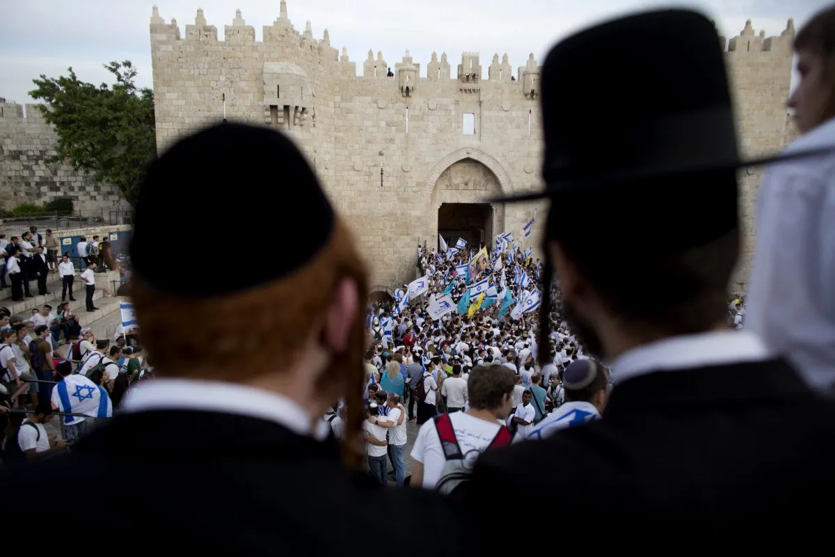 Ultra-Orthodox Jews watch people wave Israeli flags outside the Damascus Gate during Jerusalem Day celebrations in Jerusalem on May 28, 2014. (Dusan Vranic/AP Photo)