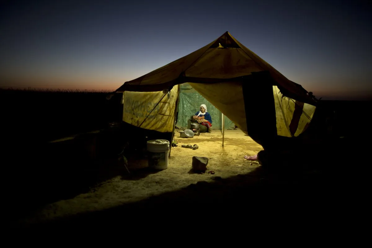 A Syrian refugee woman tends to her daughter while cooking inside her tent at an informal tented settlement near the Syrian border on the outskirts of Mafraq, Jordan, on Aug. 26, 2015. (AP Photo/Muhammed Muheisen)