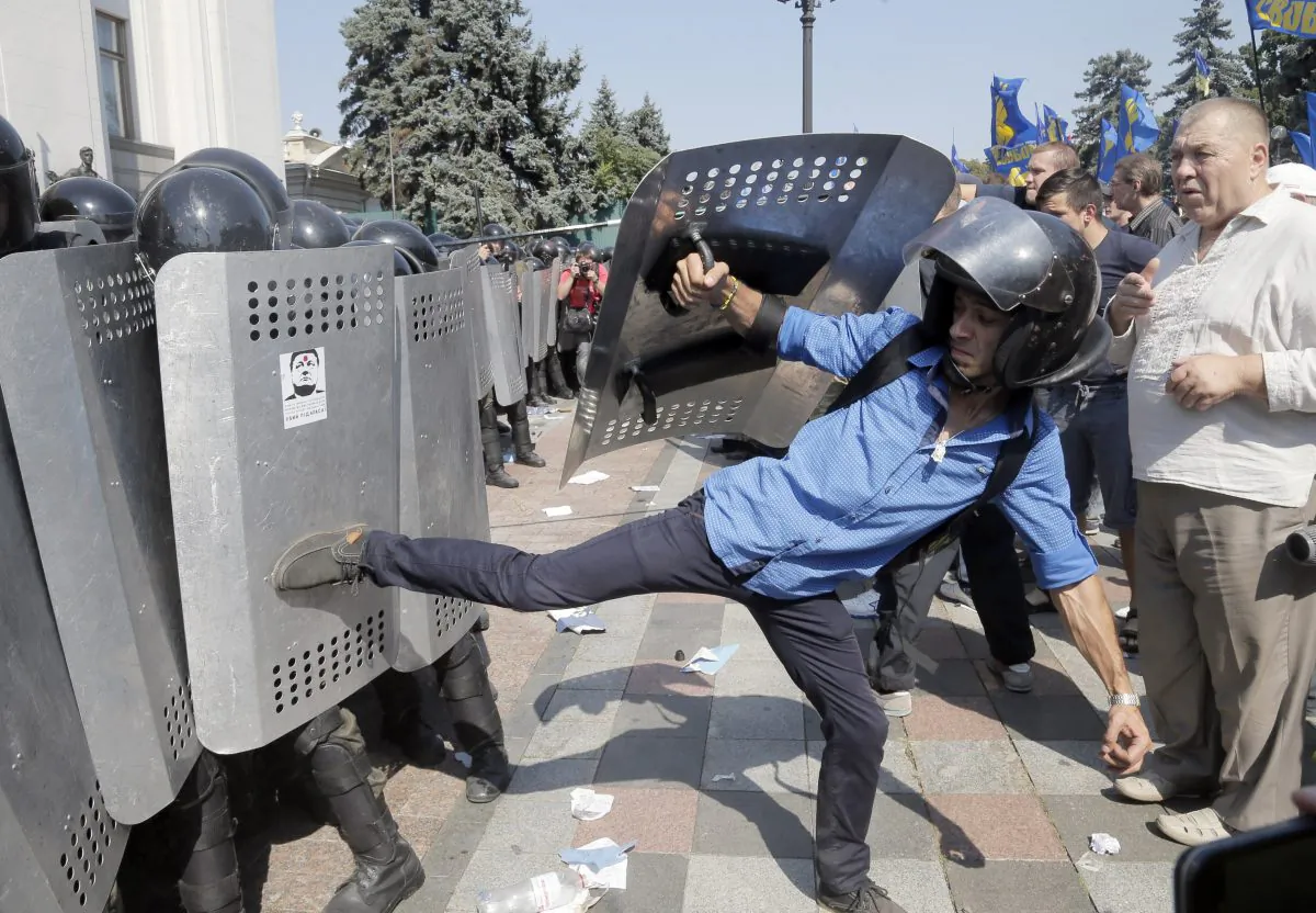 Ukrainian protesters, one using police riot equipment, clash with police after a vote to give greater powers to the east, outside the Parliament, Kiev, Ukraine, Monday, Aug. 31, 2015. The Ukrainian parliament has given preliminary approval to a controversial constitutional amendment that would provide greater powers to separatist regions in the east. Hundreds of people gathered in front of the parliament to protest against the amendment. (AP Photo/Efrem Lukatsky)