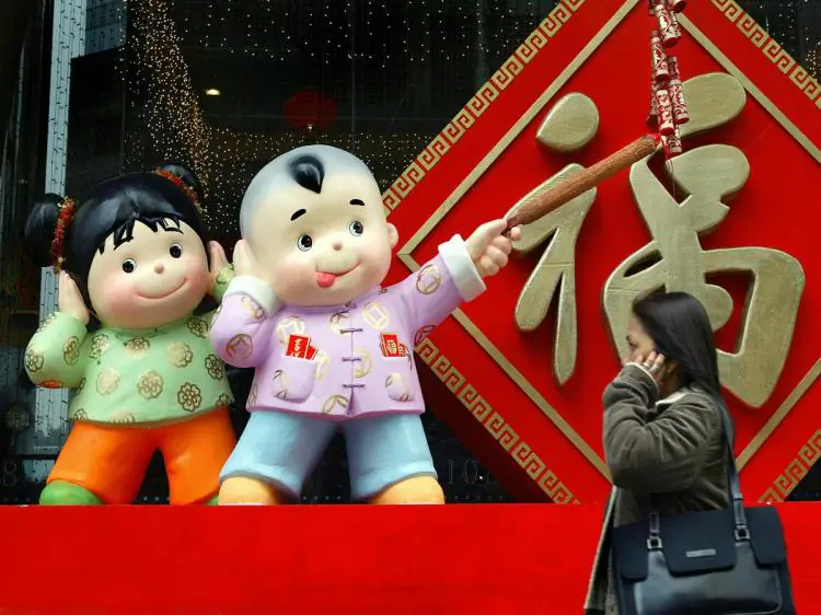 LOUD FORTUNE: A woman walks by a Chinese New Year's decoration in Hong Kong. Children are depicted lighting firecrackers decorated with wishes for good fortune. (Philippe Lopez/AFP/Getty Images)