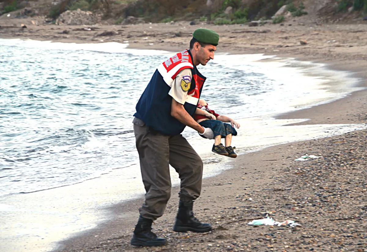 A paramilitary police officer carries the lifeless body of an unidentified migrant child, lifting it from the sea shore, near the Turkish resort of Bodrum, Turkey, early Wednesday, Sept. 2, 2015. (AP Photo/DHA)