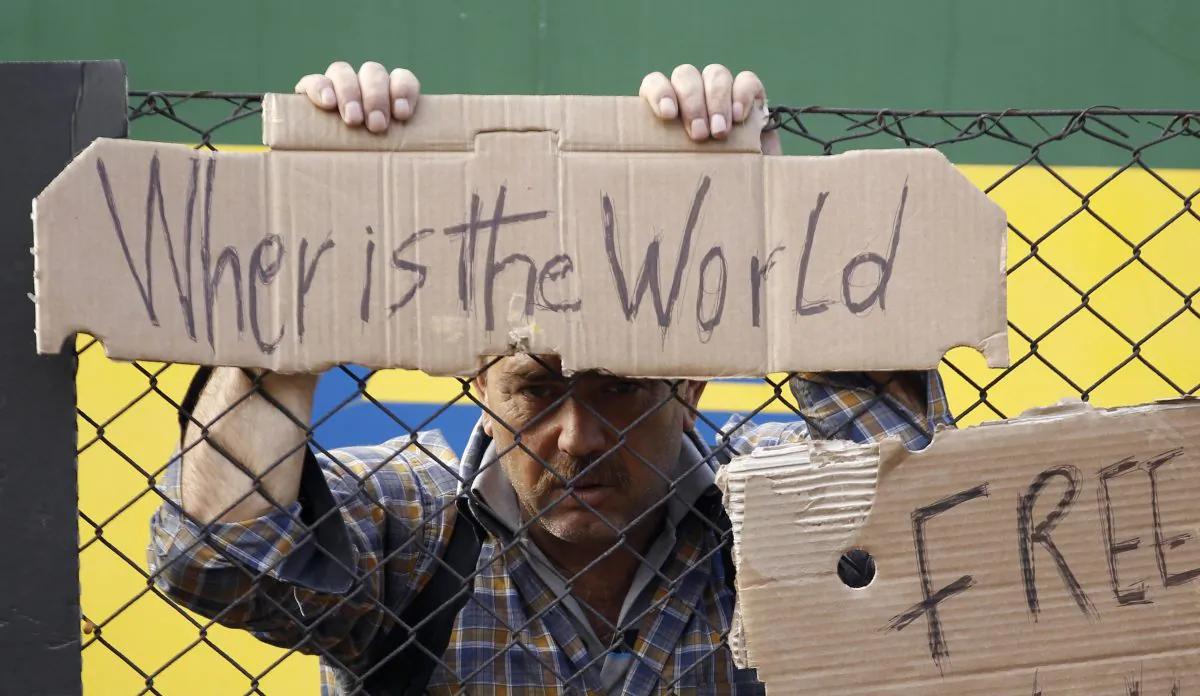 A man holds onto a fence outside a train that was stopped in Bicske, Hungary, Friday, Sept. 4, 2015. (AP Photo/Petr David Josek)