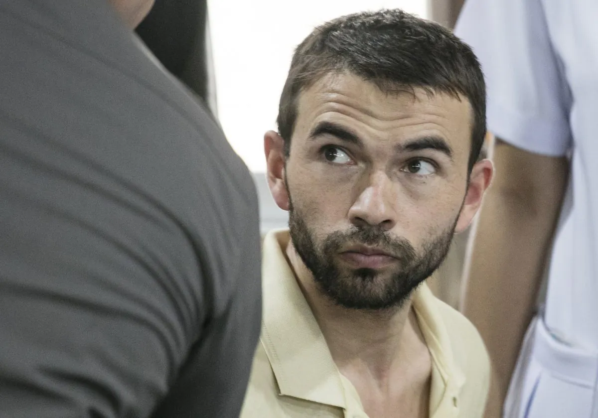 The man who was arrested at an apartment on Saturday, Aug. 29, 2015, and found with evidence police said included bomb making equipment and stacks of passports is seated after being brought to police headquarters in Bangkok, Thailand. (AP Photo/Wason Wanichakorn)