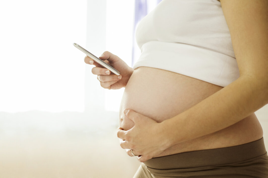 Beautiful pregnant woman with mobile phone in her bedroom