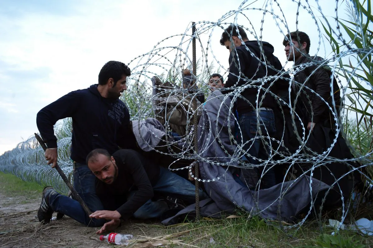 FILE - In this Wednesday Aug. 26, 2015, file photo, Syrian refugees cross into Hungary underneath the border fence on the Hungarian - Serbian border near Roszke, Hungary. A Pakistani identity card in the bushes, a Bangladeshi one in a cornfield. Documents scattered only meters from Serbia's border with Hungary provide evidence that many of the migrants flooding Europe to escape war or poverty are scrapping their true nationalities to improve their chances of asylum _ many of them claiming to be Syrian. (AP Photo/Bela Szandelszky, File)
