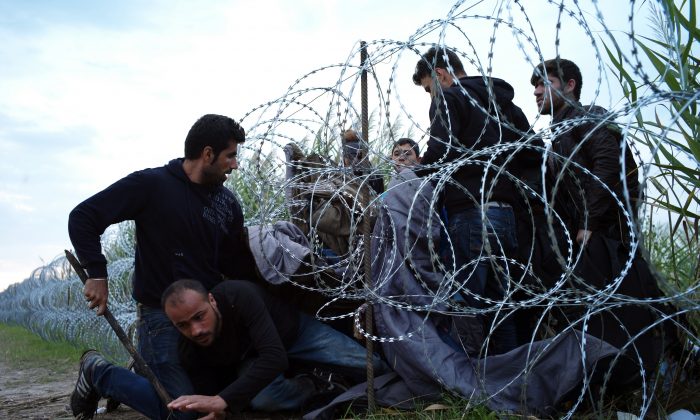 FILE - In this Wednesday Aug. 26, 2015, file photo, Syrian refugees cross into Hungary underneath the border fence on the Hungarian - Serbian border near Roszke, Hungary. A Pakistani identity card in the bushes, a Bangladeshi one in a cornfield. Documents scattered only meters from Serbia's border with Hungary provide evidence that many of the migrants flooding Europe to escape war or poverty are scrapping their true nationalities to improve their chances of asylum _ many of them claiming to be Syrian. (AP Photo/Bela Szandelszky, File)