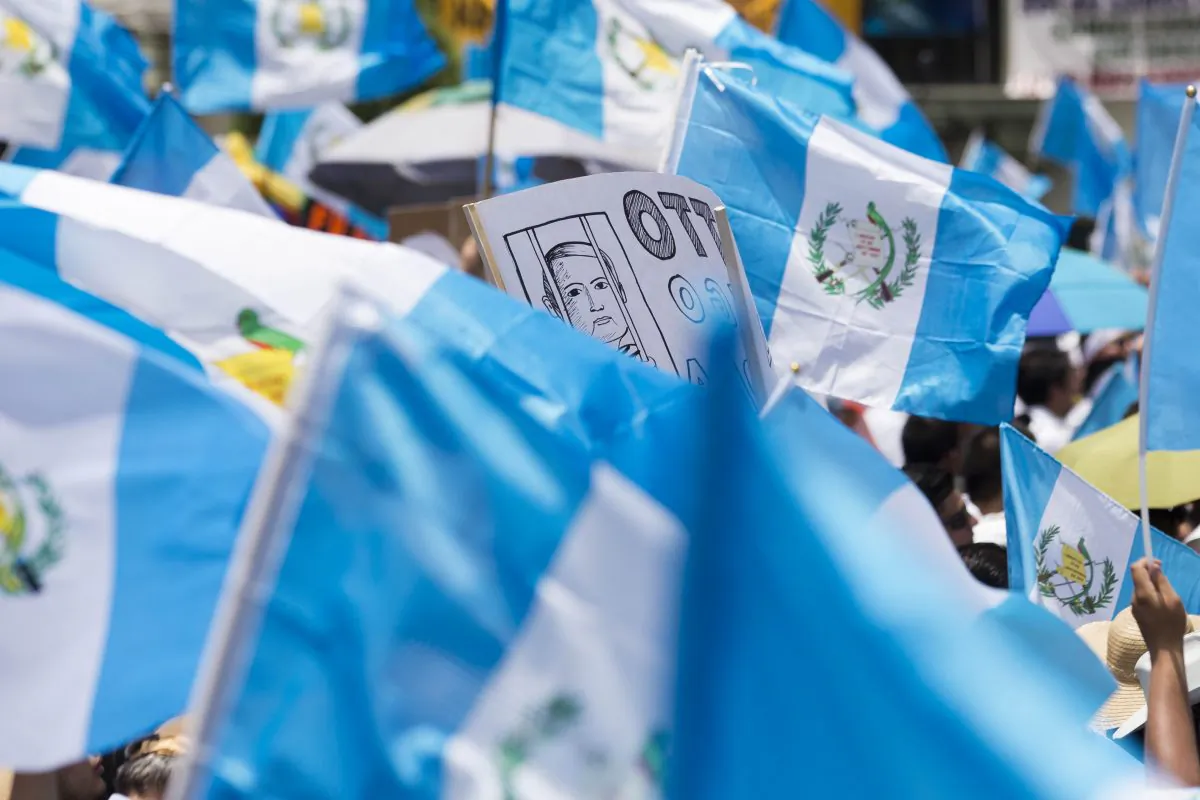 A poster with a caricature of Guatemalan President Otto Perez Molina, drawn behind bars, juts out from a sea of national flags, during a concentration of thousands calling for his resignation, gathered in front of the National Palace, in Guatemala City, on Aug. 27, 2015. (Moises Castillo/AP)
