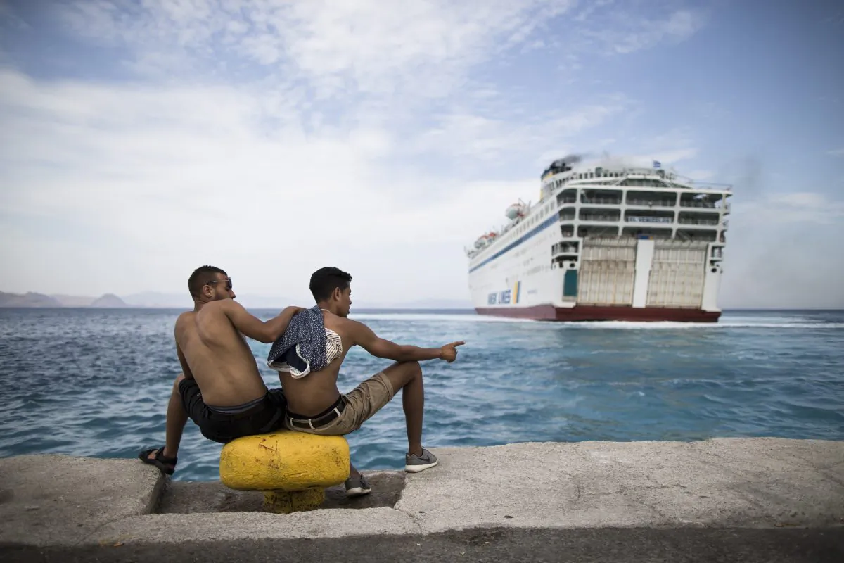 Two migrants look toward a giant passenger ferry while it arrives at the Greek holiday island of Kos, to provide temporary accommodation for some thousands of refugees sleeping rough after crossing clandestinely from Turkey in flimsy boats, Greece, Friday, Aug. 14, 2015. (AP Photo/Alexander Zemlianichenko)
