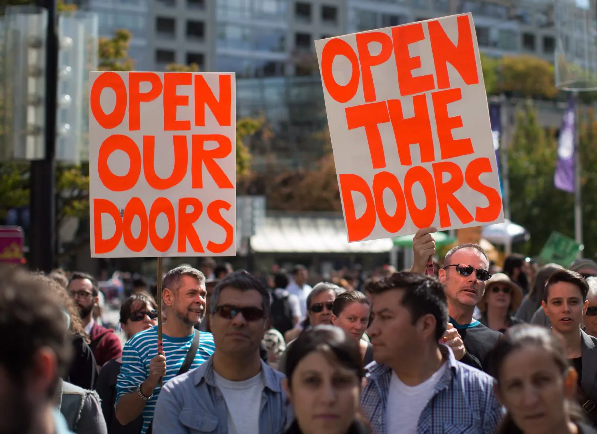 Two men hold signs as hundreds gather for a rally on Sept. 6, 2015 in Vancouver organized by the local Kurdish community to urge the federal government to allow more Syrian refugees into the country. Provincial calls for Canada to accept more Syrian refugees fail to address the crucial question of who would foot the bill, says an immigration expert. (The Canadian Press/Darryl Dyck)