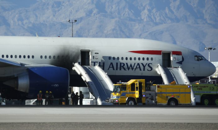 Firefighters stand by a plane that caught fire at McCarren International Airport, Tuesday, Sept. 8, 2015, in Las Vegas. An engine on the British Airways plane caught fire before takeoff, forcing passengers to escape on emergency slides. (AP Photo/John Locher)