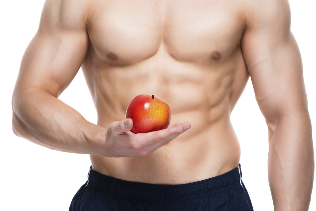 Young man with perfect body holding red apple in his hand - isolated on