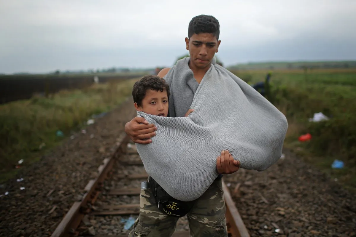 A youth carries a young boy in a makeshift sling as migrants walk towards waiting buses at the Hungarian border with Serbia on September 11, 2015 in Roszke, Hungary. (Christopher Furlong/Getty Images)
