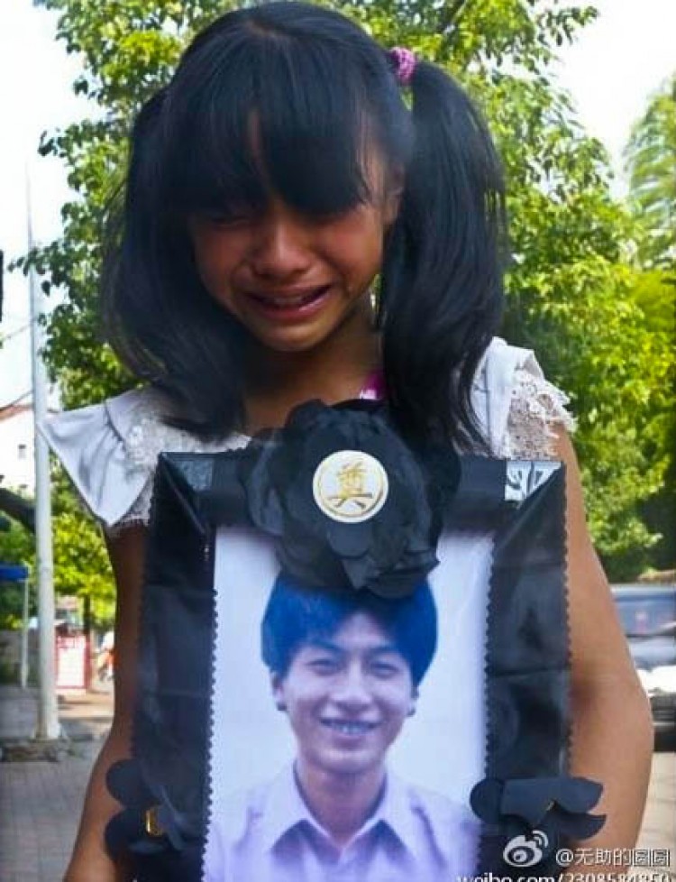 Sobbing 10-year-old child holds the funerary photo of her father, Huang Guohui.  (Weibo.com)